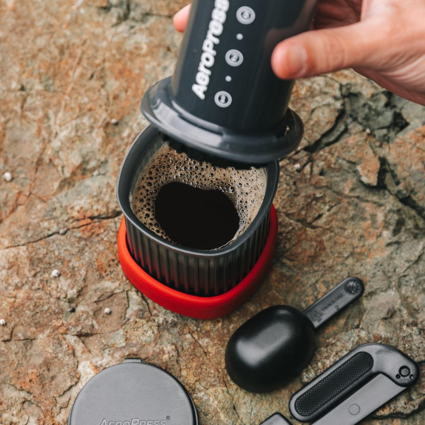A person using an AeroPress to make coffee on a stone surface.