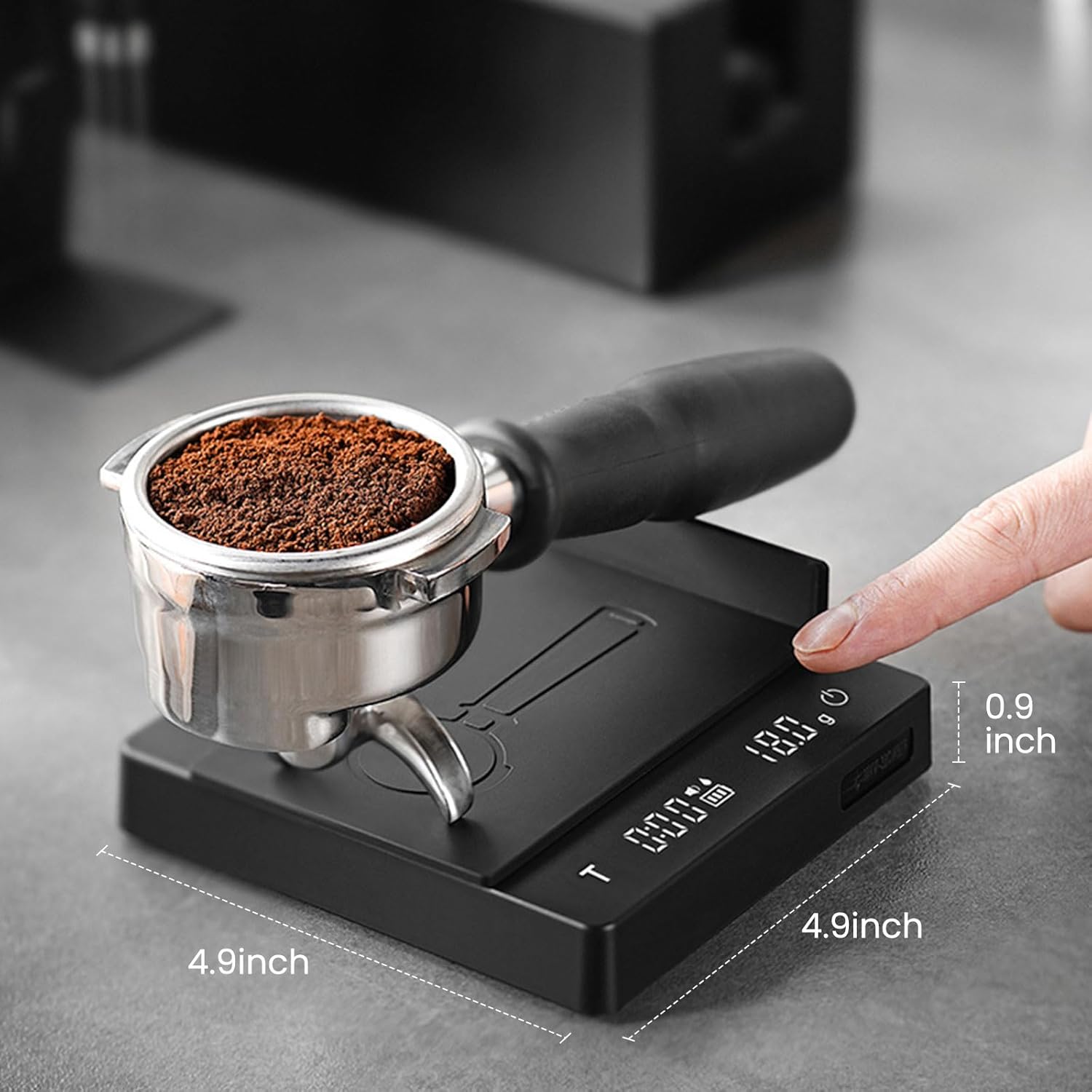 Coffee grinder with digital display on a gray surface, showing coffee grounds and a finger pointing at the display.