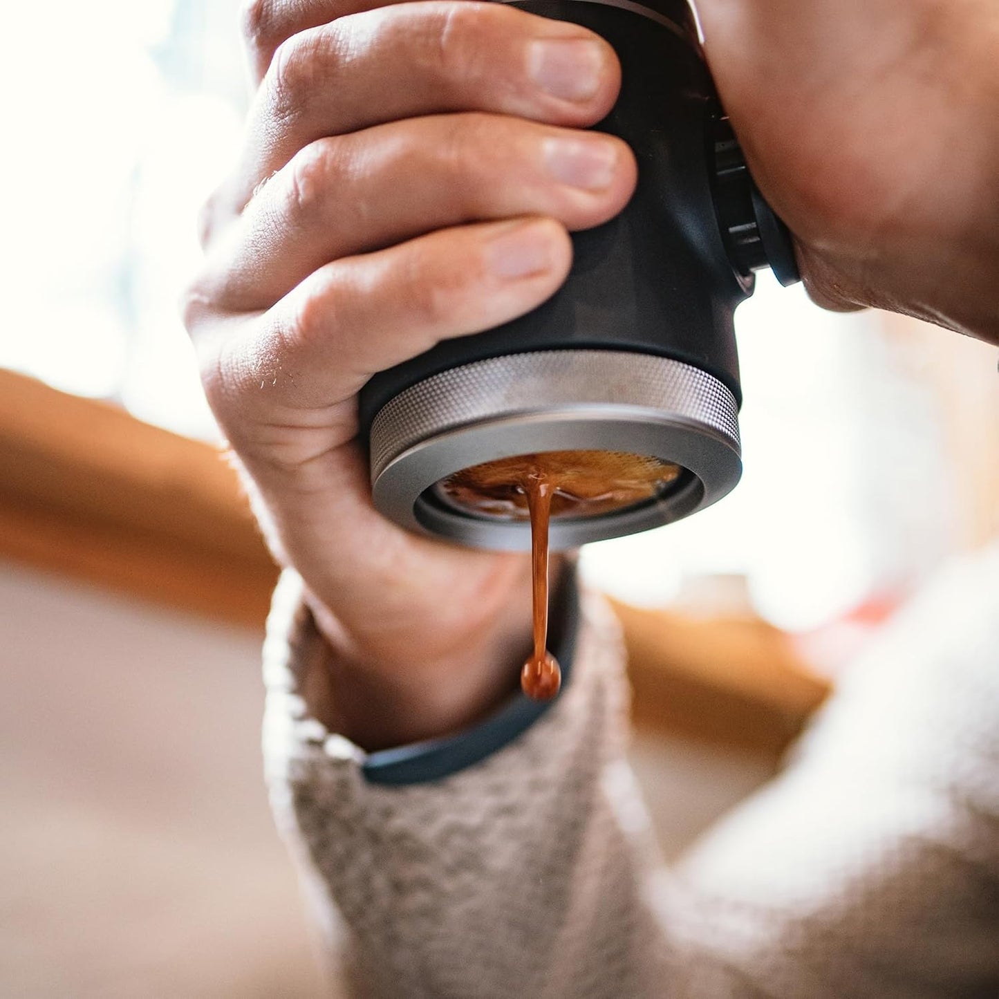 Hand holding a portable coffee maker with coffee dripping, blurred background
